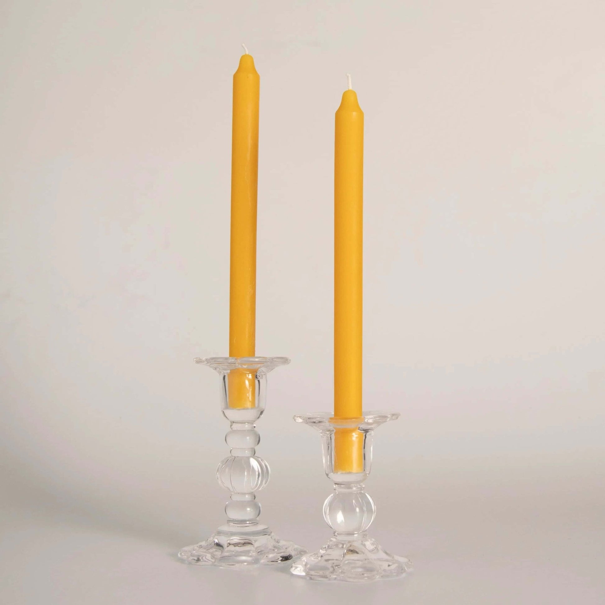 Deux bougie plus précisément "Deux cierges" en cire d'abeille jaunes, faits artisanalement à la main en Gaspésie, Québec par Florimel & Cie , placés dans des bougeoirs en verre transparent.