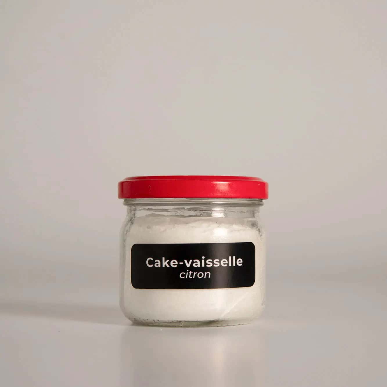 Pot de "Cake-vaisselle citron" écologique en verre avec couvercle rouge. Produit naturel, économique et efficace pour laver la vaisselle.