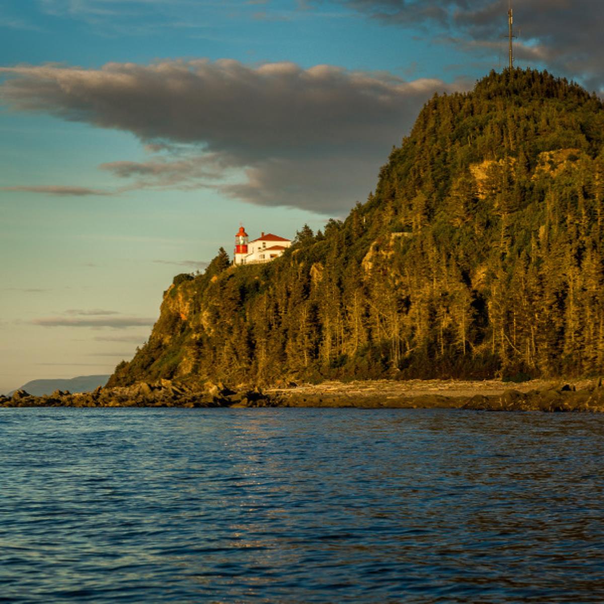 Camping du Phare à Cap-Chat en Gaspésie, Québec, avec vue sur un phare pittoresque perché sur une falaise boisée au bord de la mer.